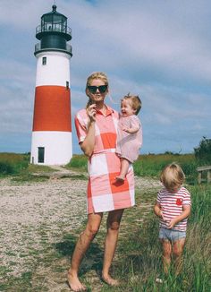 a woman and child standing in front of a light house with a red and white checkered dress