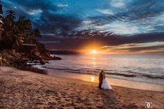 the bride and groom are standing on the beach as the sun sets in the background