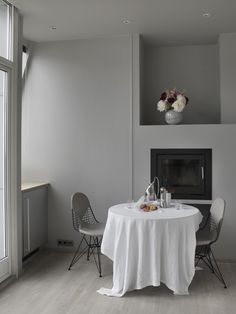 a table with two chairs and a white table cloth on it in front of a fireplace