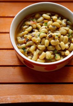 a white bowl filled with beans on top of a wooden table next to a spoon