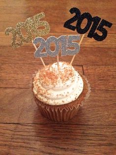 a cupcake topped with white frosting and gold sprinkles sitting on top of a wooden table