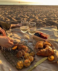 two people are sitting on the beach with some food and wine in front of them