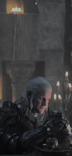 the white haired man is sitting at a table in front of candles and looking down