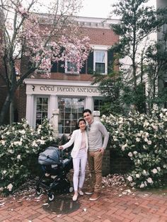 a man and woman standing next to a baby carriage in front of a flowered building