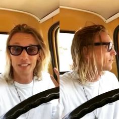 a man with long hair and sunglasses sitting in a bus looking at the camera while holding his hand up