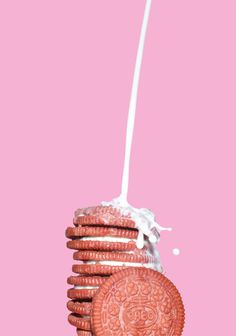 an oreo cookie with milk being poured into it on top of pink background,