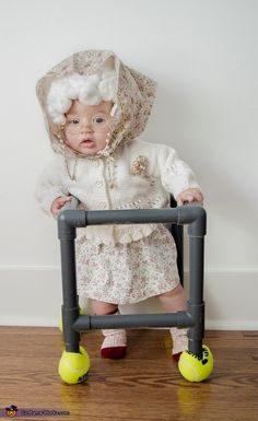 a small child wearing a bonnet and sitting in a chair with yellow rubber balls on the floor