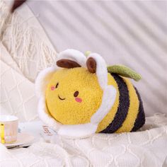 a small stuffed bee sitting on top of a bed next to a cup and saucer