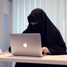 a woman wearing a black hijab sitting in front of a laptop on a desk