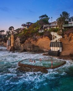 people are swimming in the ocean next to a cliff with houses and cliffs on it