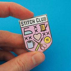 a hand holding a pink and white pin with sewing related items on it's back