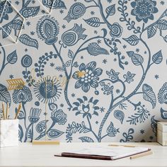 a blue and white floral wallpaper with gold accents on a desk next to a book