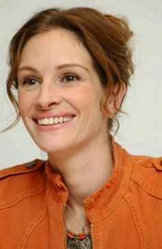 a smiling woman in an orange shirt with a necklace on her neck and hair pulled back