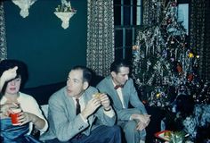 three people sitting on a couch in front of a christmas tree eating food and drinking