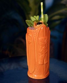 an orange drink sitting on top of a table next to a potted green plant