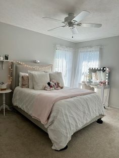 a bedroom with a white bed and pink comforter on top of it, along with lights strung from the ceiling