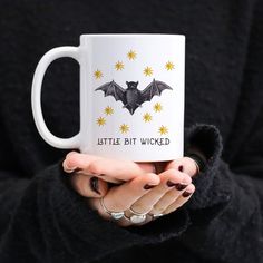 a woman holding a white coffee mug with a bat on it that says, little bit woked