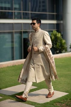 a man walking across a grass covered field wearing a white suit and brown shoe shoes