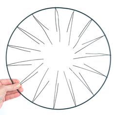 a hand drawing a circular object with black marker on a white surface, in the shape of a sunburst