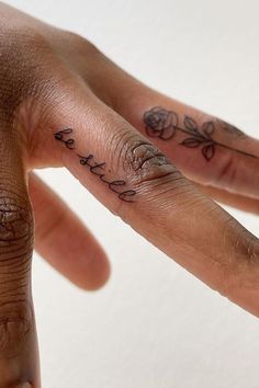 a person's hand with two fingers that have tattoos on them and the words love is written in cursive writing