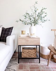 a white couch sitting next to a table with a basket on it and a vase filled with flowers