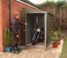 a man standing next to a motorcycle in a storage shed with the door open and his motorbike parked inside