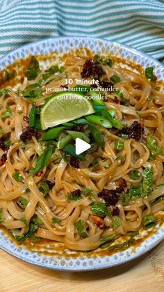 a white bowl filled with noodles and vegetables on top of a wooden table next to a fork