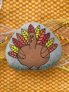 a turkey painted on a rock sitting on top of a checkered tablecloth covered surface