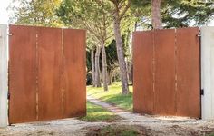 two wooden gates open in the middle of a dirt path with trees and grass behind them