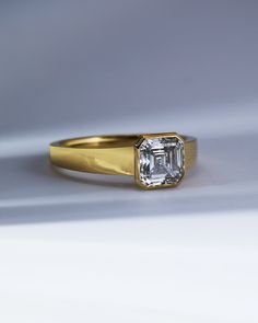 a gold ring with an emerald cut diamond in the center on a white background,