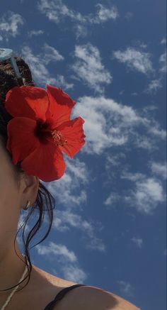 a woman with a red flower in her hair looking up at the blue sky and clouds