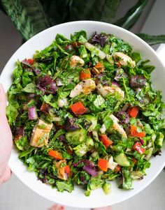 a person holding a white bowl filled with salad