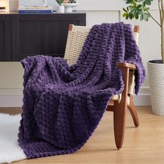 a purple blanket sitting on top of a wooden chair next to a potted plant