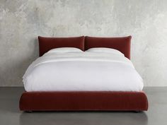 a bed with white sheets and red headboard in front of a concrete wall,