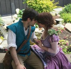 a man and woman dressed up as disney characters sitting on a stone bench in front of a garden