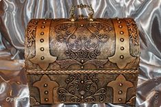 a brown leather box with intricate designs on it's sides and handles, sitting on a shiny surface