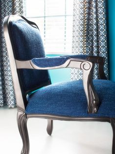 a blue upholstered chair in front of a window with curtains and drapes