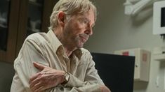 an older man sitting at a desk with his arms crossed and looking off to the side