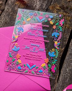 a pink and blue wedding card on top of an envelope