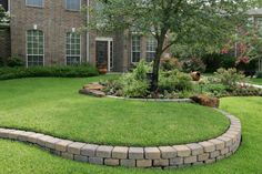 a large yard with grass and landscaping in front of a brick house on a sunny day