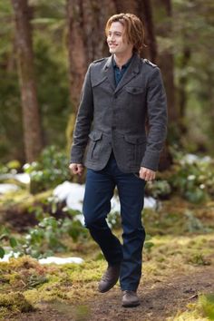 a man walking in the woods wearing a jacket and pants with his hands in his pockets