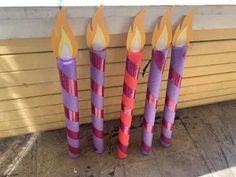 three purple candles with orange and pink stripes on them sitting in front of a building