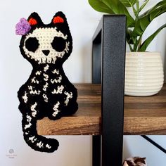 a crocheted cat sitting on top of a wooden table next to a potted plant