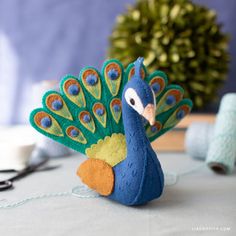 a blue and green peacock sitting on top of a table next to scissors, thread and yarn