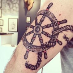 a man's arm with a ship wheel tattoo on it