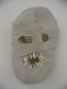 a white mask with holes in the middle and teeth on it's face, hanging from a wall