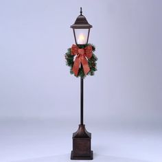 a lamp post with a wreath on it and a lit candle in the middle, against a white background