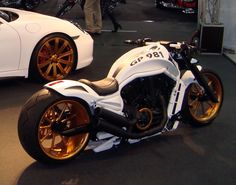 a white motorcycle with gold rims parked next to a white car in a showroom