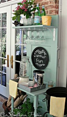 a shelf filled with lots of bottles and glasses on top of a wooden table next to a door