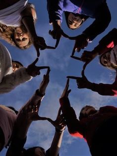 a group of people standing in a circle with their hands together and looking up at the sky